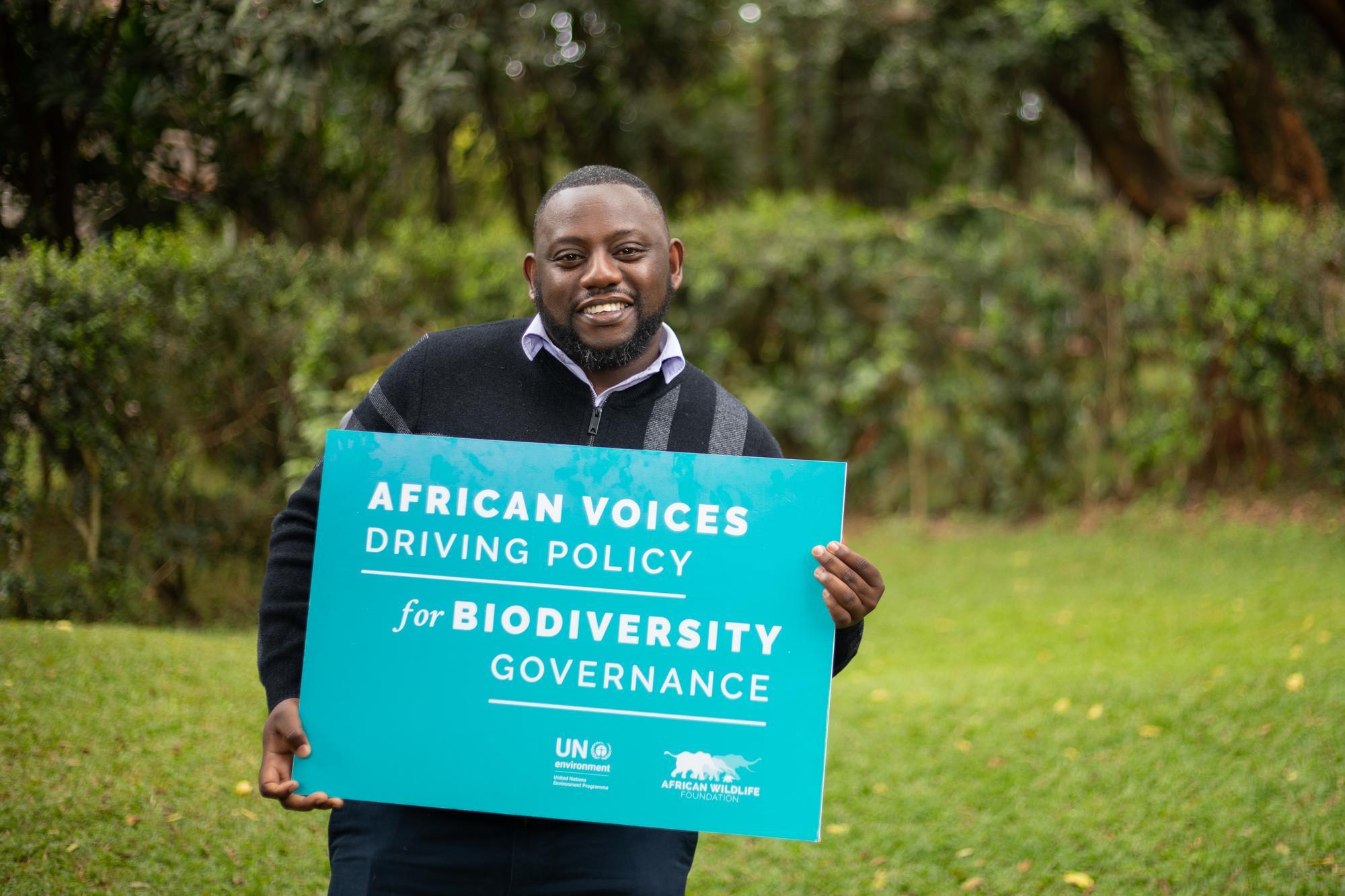 Youth fellow holds a sign saying "African Voices Driving Policy for Biodiversity Governance"