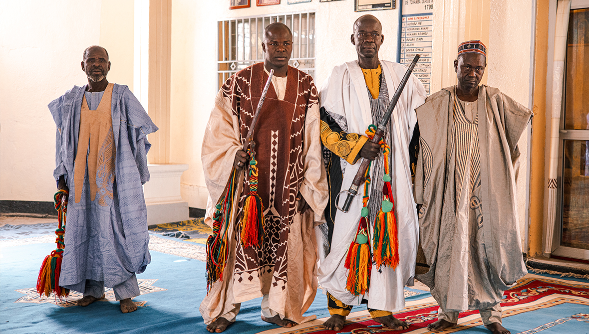 Four men wearing ornate patterns stand in the Lamido's court.