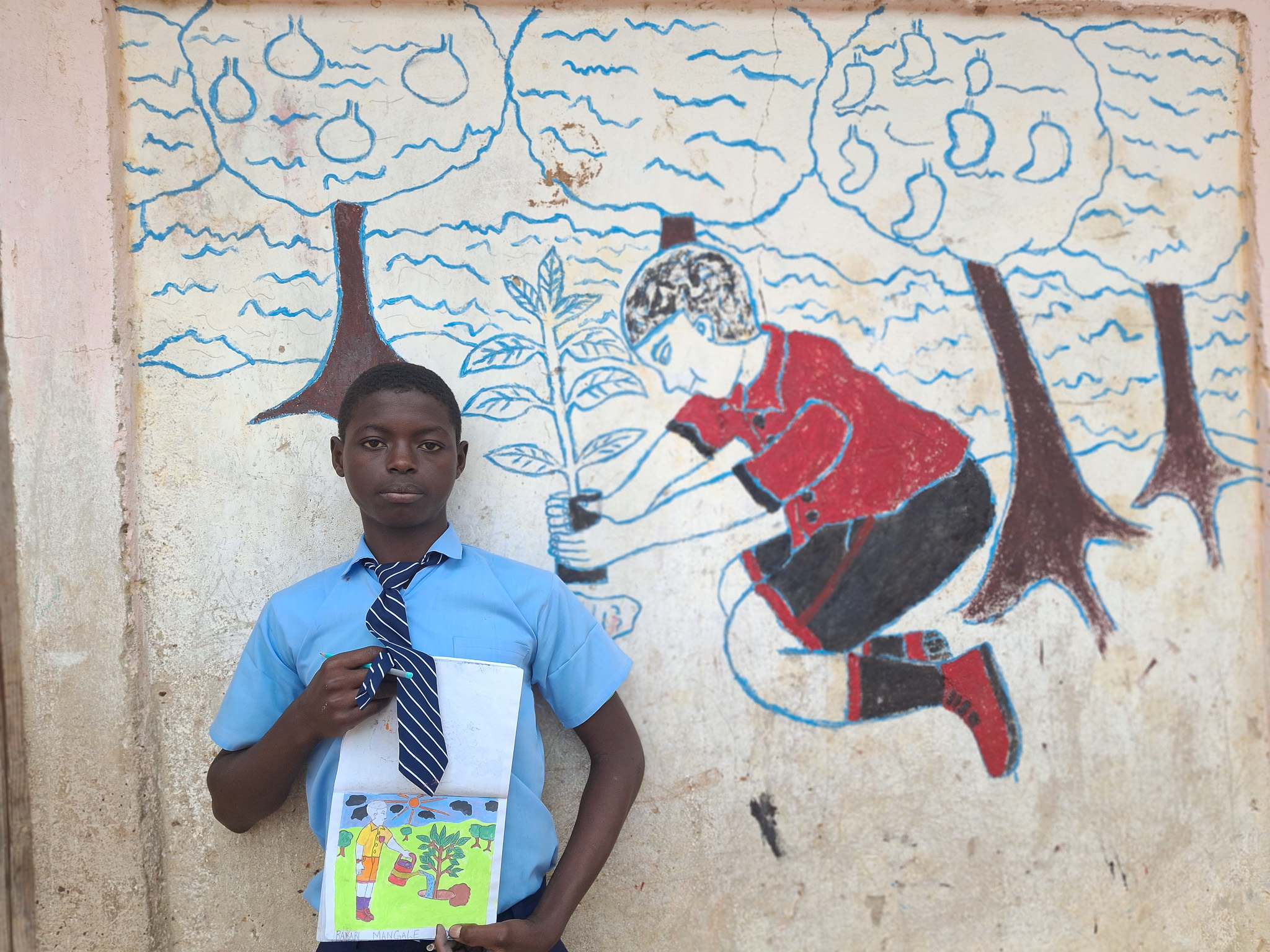 Bakari showcasing some of his artwork, including a drawing and a wall mural.