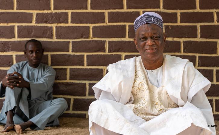 Medium shot of two men sitting in front of a brick wall.