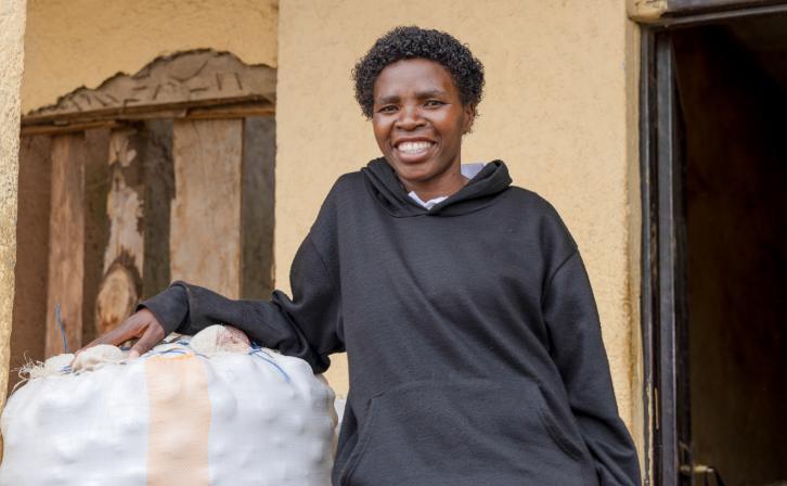 Mukarwego Agnes standing beside stored Irish potatoes, a key commodity in her agribusiness.