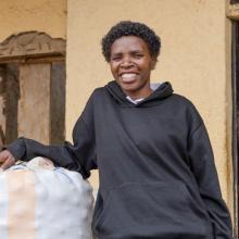 Mukarwego Agnes standing beside stored Irish potatoes, a key commodity in her agribusiness.